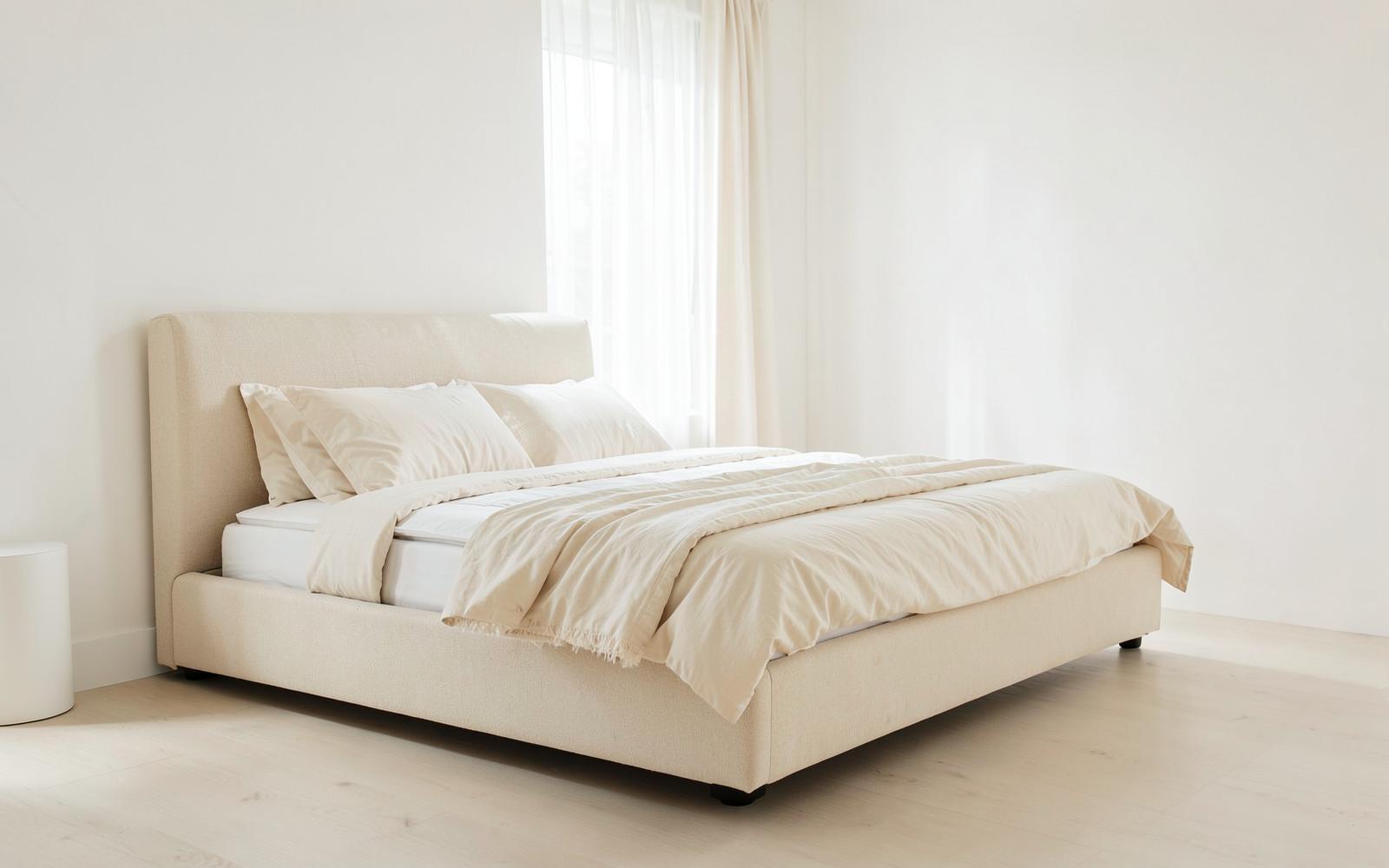 Cama estofada com colchão e roupa de cama em tons crus